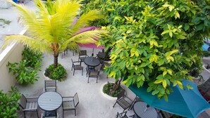 Ein Terrassenbereich im Freien mit runden Tischen und Stühlen, umgeben von Pflanzen und einem großen Sonnenschirm.