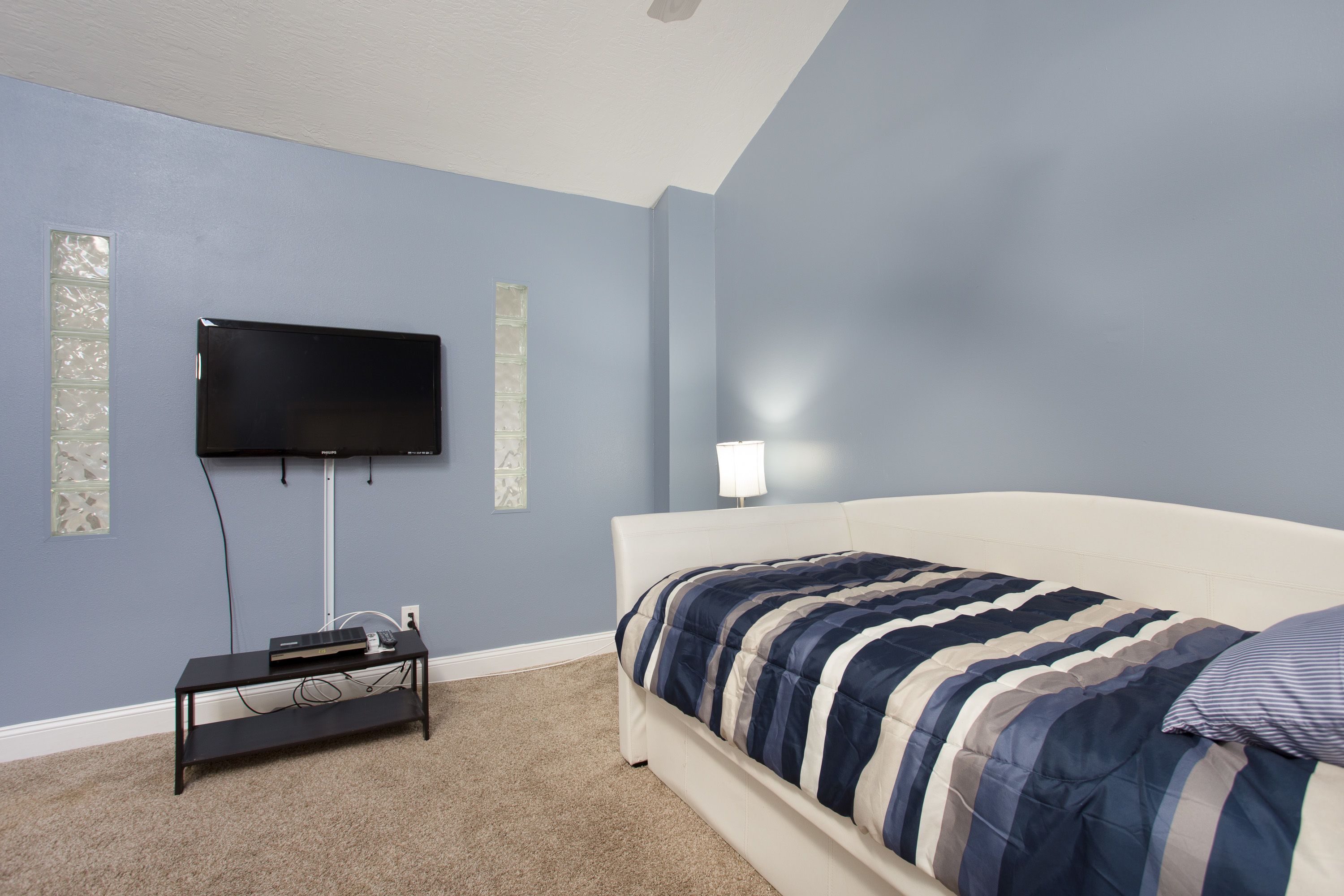 A bedroom with a bed, a TV mounted on the wall, a bedside table, and a lamp.