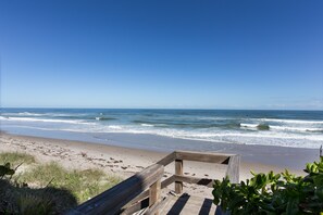 A wooden boardwalk leading to a sandy beach with ocean waves. - Coastal Tides (Melbourne Beach)
