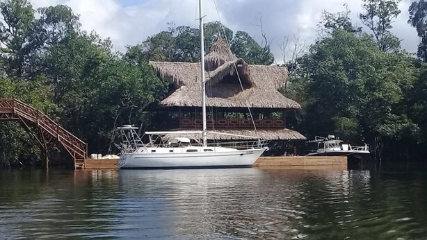 A white yacht docked at a pier with a thatched-roof structure nearby. - Tenamit Maya (Livingston)