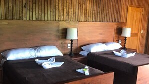 A hotel room with two wooden beds, each with a pillow and a folded towel. There are two bedside lamps and a wooden door. - Tenamit Maya (Livingston)
