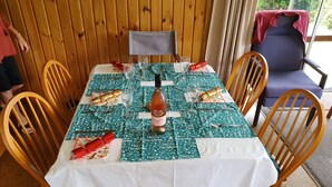A dining table set with a bottle of wine, glasses, and wrapped gifts, surrounded by wooden chairs. - Ngakuta Bay, Marlborough Sounds. (Ngakuta Bay)