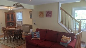 Sala de estar con sofá rojo, mesa de comedor de madera y sillas. Se observa una escalera con barandilla que conduce a otro nivel.