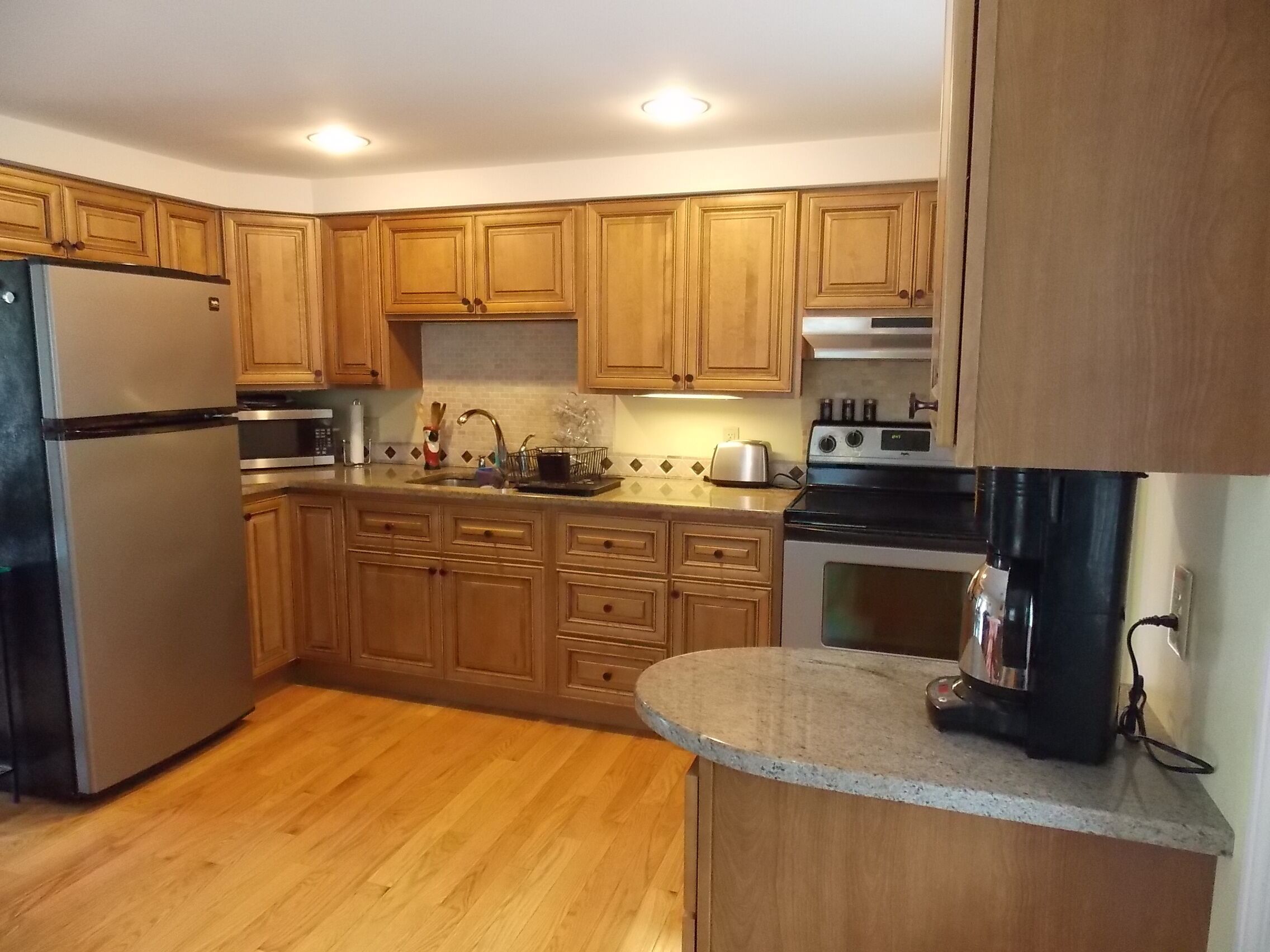A kitchen with wooden cabinets, a stainless steel refrigerator, a stove, and a microwave.