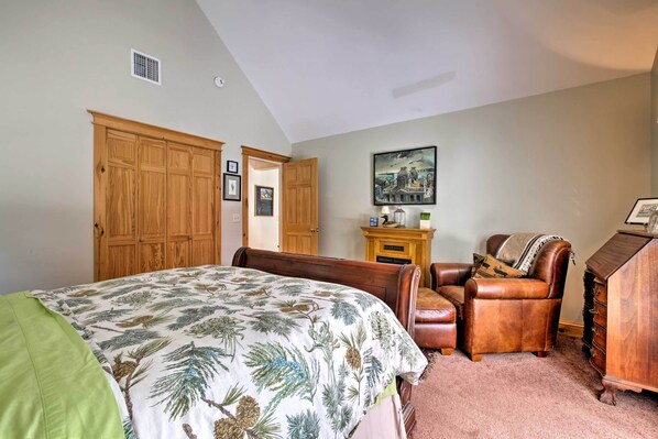 A bedroom with a large bed, a wooden wardrobe, a leather armchair, and a dresser. - Hot Tub, Dock, View! Waterfront Great Pond Cottage (Great Pond)