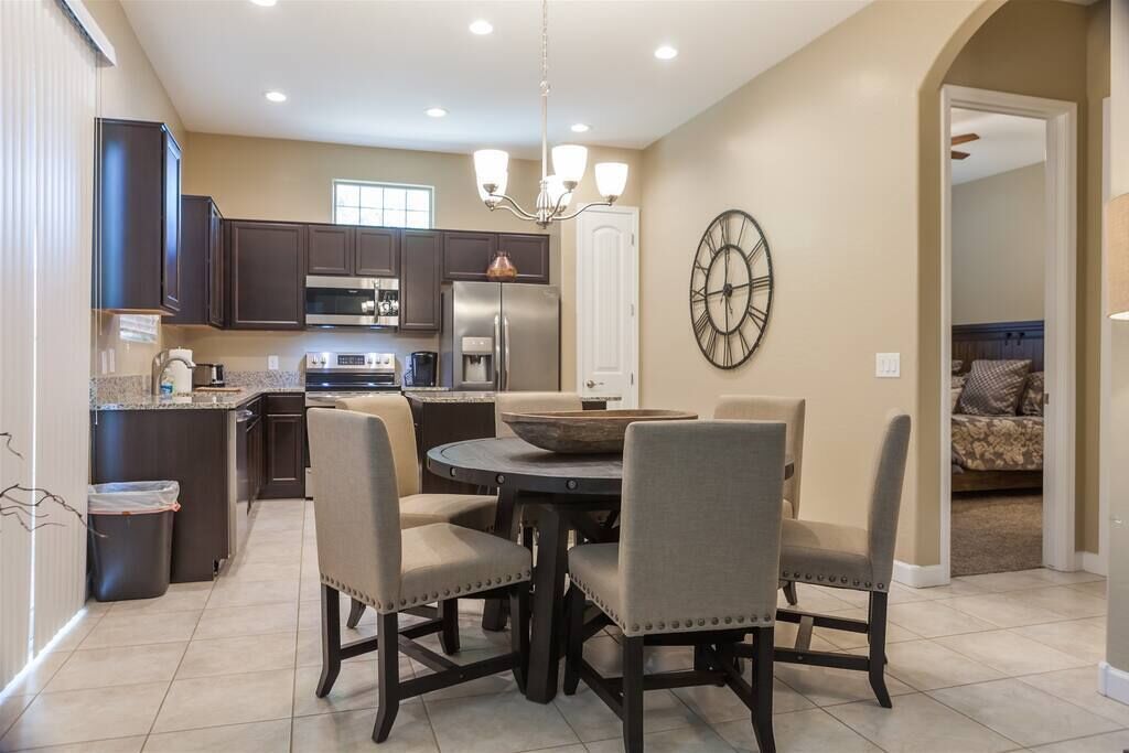 A modern kitchen with dark cabinets, a stainless steel refrigerator, and a dining area with four chairs and a round table.