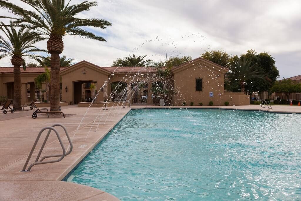 A swimming pool with a water feature, palm trees, and a building with a tiled roof.
