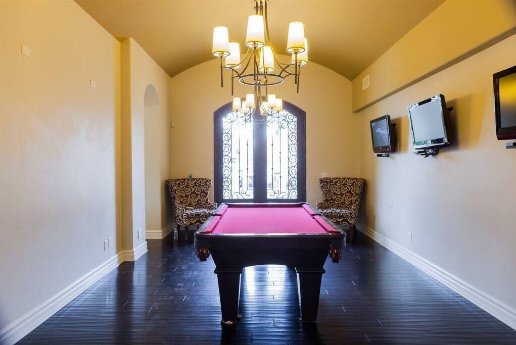 Une table de billard dans une pièce où se trouvent des chaises à motifs, un lustre et une grande fenêtre.