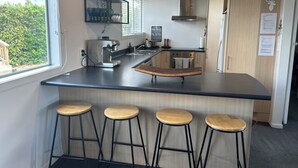 A modern kitchen with a central island, bar stools, a built-in oven, and a view of greenery outside. - Trout Retreat - Mountain, lake and river (Turangi)