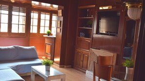 A cozy living room with a sofa, a coffee table with a plant, wooden cabinets, and a TV mounted on the wall. - Duplex of 90m2, 6 persons with terrace of 30m2 (Barcelona)