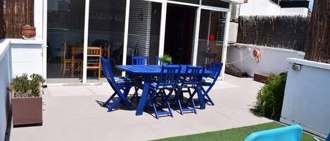A patio with a blue table and chairs, a covered seating area, and artificial grass.
