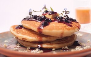 A stack of pancakes with syrup and blueberries on a plate. - Willka T'ika Essential Wellness (Urubamba)