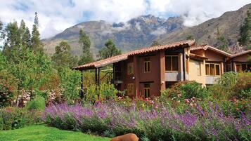 Set amidst lush greenery and mountains, this traditional house offers a serene retreat with a balcony and stone wall.