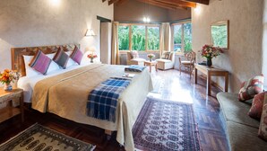 A spacious bedroom with a large bed, a sitting area with a view of greenery, and a dining area with a table and chairs. - Willka T'ika Essential Wellness (Urubamba)