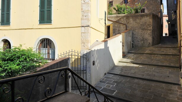 A narrow stone staircase leading up to a building with a yellow facade and green shutters.