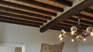 A room with exposed wooden beams, a chandelier, a bed with floral bedding, and a dresser.