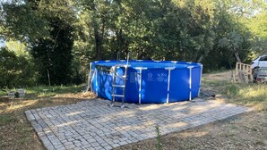 Een blauw bubbelbad met een trap, omgeven door een terras van bakstenen en bomen.