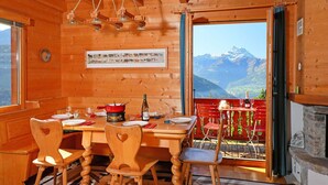 Une salle à manger en bois avec une table dressée pour deux personnes, une cheminée et une vue sur les montagnes.