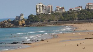 A beach with people, a rocky outcrop, and buildings in the background. - Luxury studio 1st line Ocean for 2 persons (Biarritz)