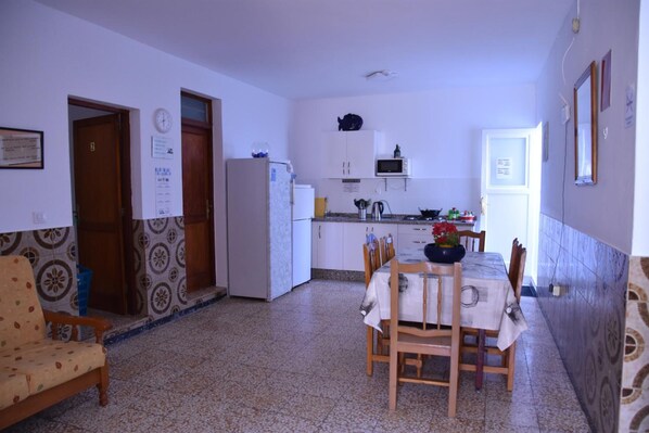 A compact kitchen with a refrigerator, microwave, and sink. There is a dining table with chairs and a patterned wall.