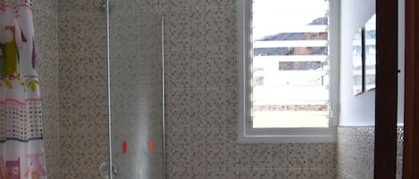 Een badkamer met een douche, toilet en een raam.