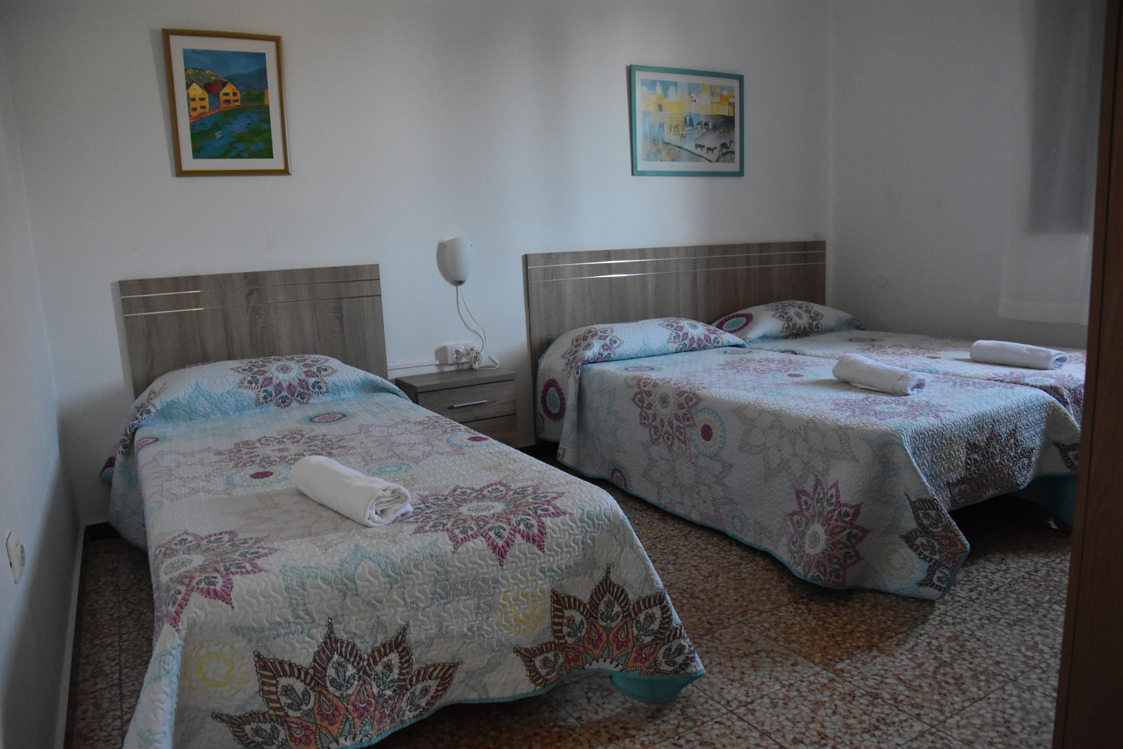 Habitación de hotel con dos camas, cada una con una colcha estampada y una toalla enrollada. Hay dos mesitas de noche con lámparas y un teléfono en la pared.