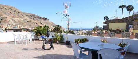 Un patio al aire libre con una mesa, sillas, una máquina de coser y vistas al mar y las colinas.