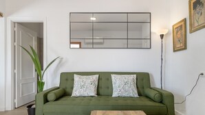 A green sofa with floral pillows, a wooden coffee table, a large mirror, and a floor lamp.