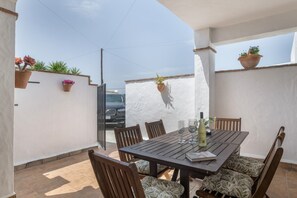 A patio with a wooden table and chairs, potted plants, and a car in the background.