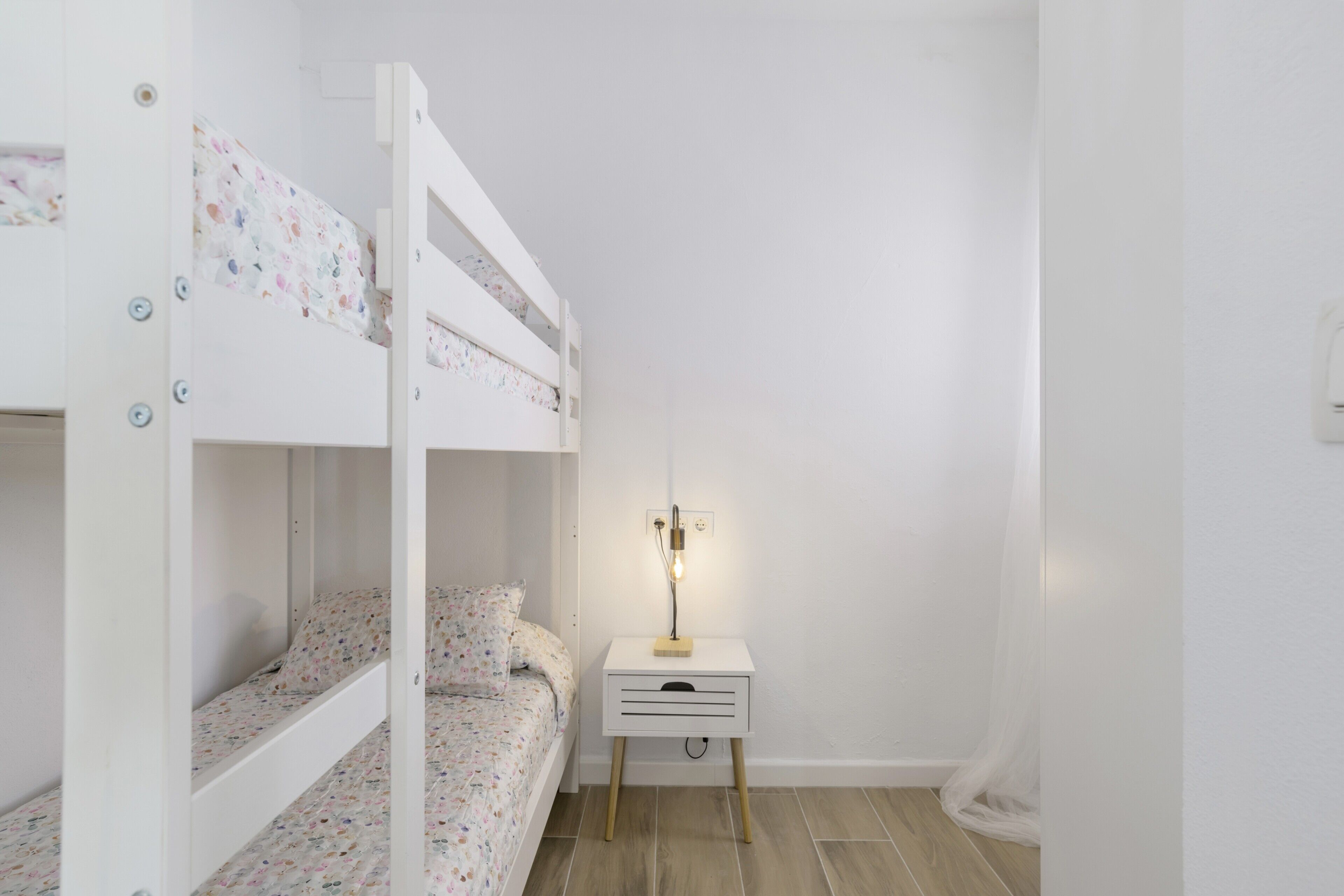 Una cama individual con ropa de cama estampada, una mesita de noche con lámpara y una pequeña cómoda.