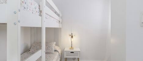 Una cama individual con ropa de cama estampada, una mesita de noche con lámpara y una pequeña cómoda.