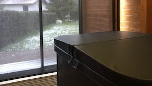 Quarto com hidromassagem, janelas amplas, vigas de madeira no teto e vista para o exterior.