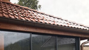 Uma casa com uma grande porta de correr de vidro, telhado em cerâmica e deck de madeira.