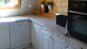 Uma cozinha com armários brancos, lava-louças, forno e janela com persianas.