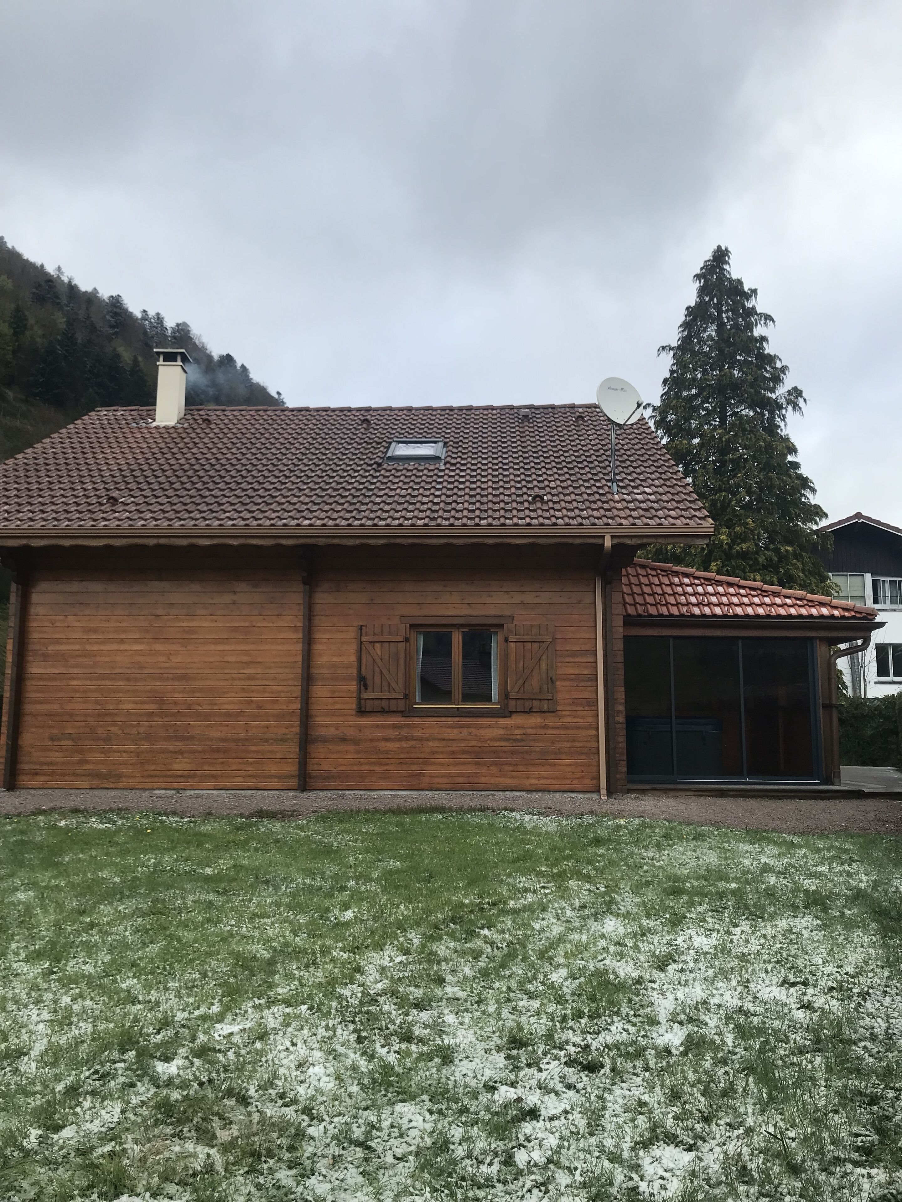 A wooden house with a tiled roof, a chimney, and a satellite dish.