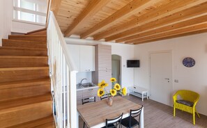 A modern kitchen with wooden beams, a dining area with a table and chairs, and a staircase.