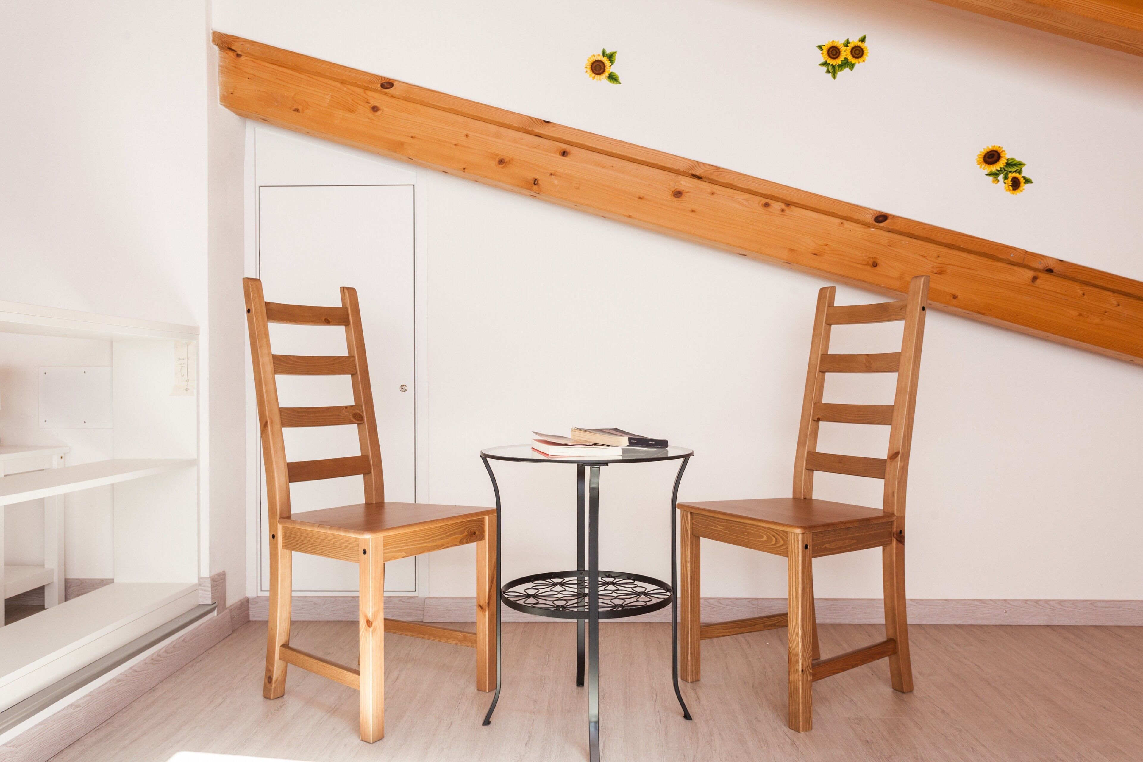 Ein Zimmer mit zwei Holzsesseln, einem kleinen runden Tisch und einer weißen Tür.