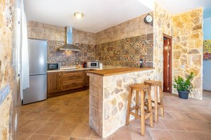 Eine Küche mit Steinrückwand, Holzbarhocker, einem Kühlschrank, einer Mikrowelle und einem Spülbecken.