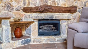 Une cheminée en pierre avec un feu de bois, une étagère avec un pot et un fauteuil rembourré.