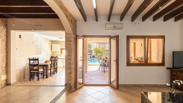 Uma sala de estar ampla com um conjunto de jantar, uma porta de vidro que dá para o exterior e uma televisão sobre um móvel.
