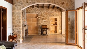 Um quarto com paredes de pedra, lareira, prateleiras de madeira e uma porta que dá para outra área.