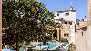 Área de piscina com espreguiçadeiras, uma mesinha e uma árvore com frutos.