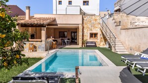 Piscina com espreguiçadeiras, área de estar com móveis de exterior e escadaria para um edifício.