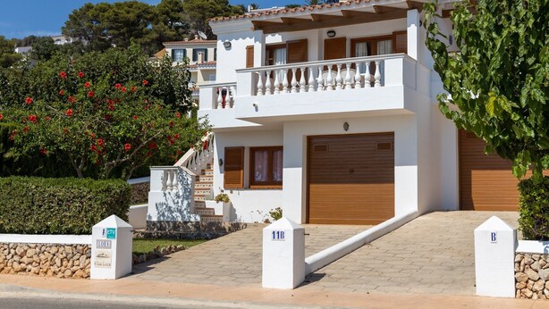 A two-story villa with a balcony, a garage, and a stone wall.