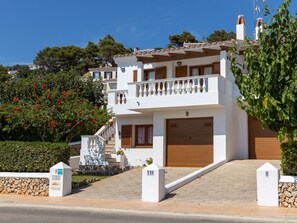 Una villa a due piani con un balcone, un garage e un muro in pietra.
