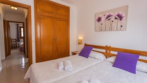 A bedroom with a bed, two pillows, a nightstand, a wall-mounted lamp, and a door leading to another room.