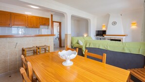 A compact kitchen with wooden cabinets, a dining table with chairs, a sofa, and a fireplace.