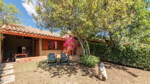 Una casa con un patio, due sedie, un tavolo e un albero con fiori rosa.