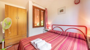 Una camera da letto con un letto, un armadio, una finestra, un comodino e una ventola.