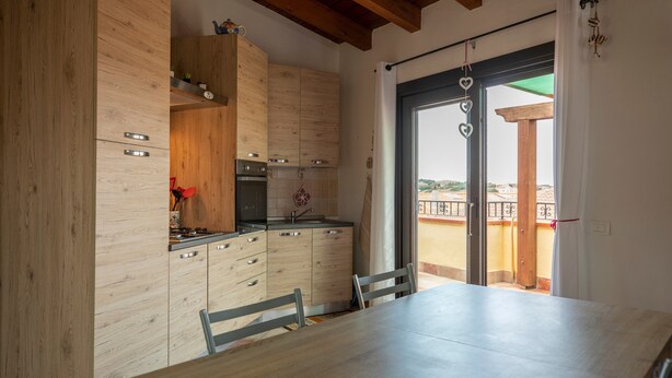 Een moderne keuken met houten kastjes, een eettafel en een uitzicht door een glazen deur op een buitenbalkon.